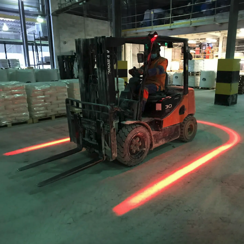 Forklift in a warehouse environment with a red line light projected on the floor.