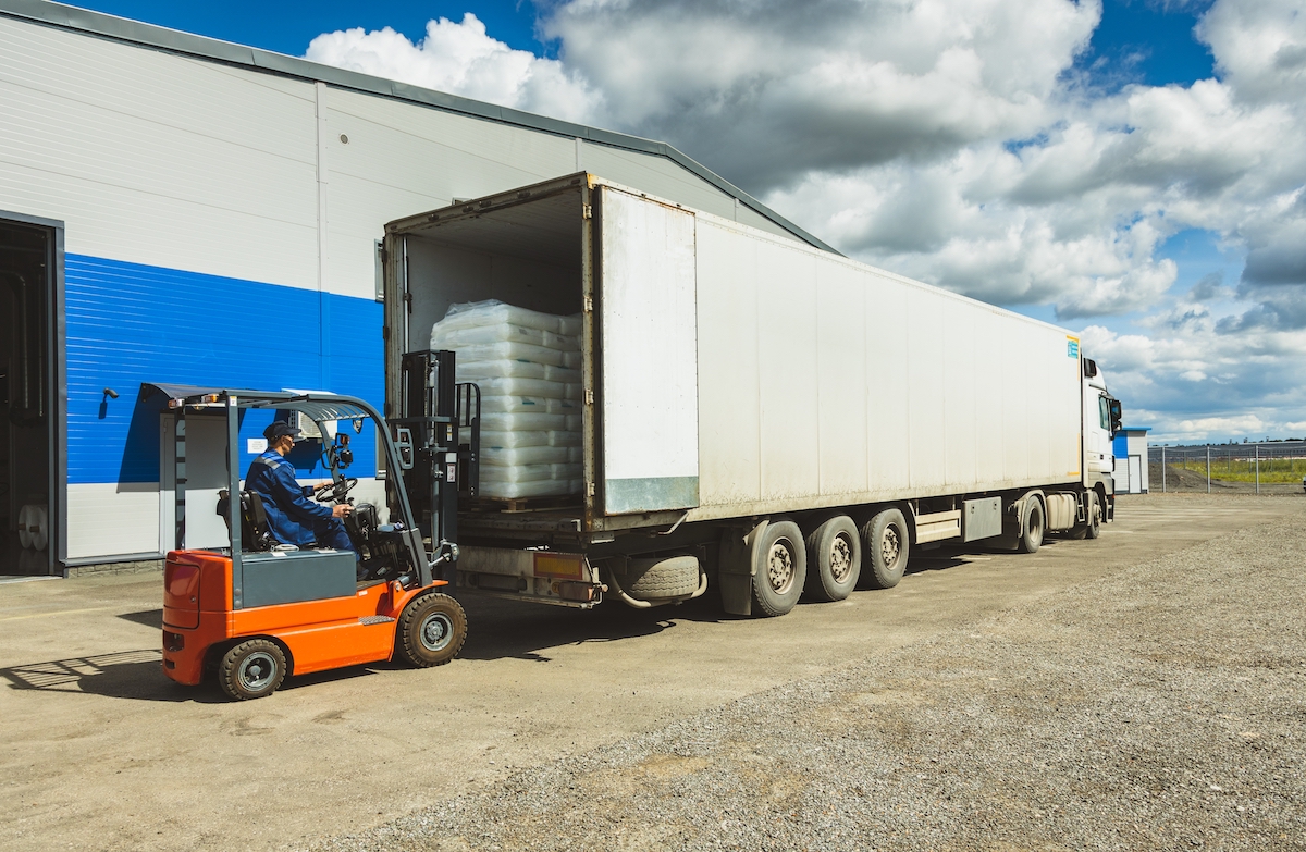 Forklift operator loading palletised goods into refrigerated articulated lorry at warehouse loading bay.