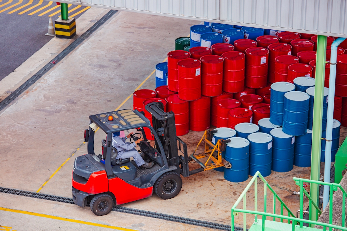 Red forklift truck transporting industrial drums in outdoor storage yard showing materials handling operations