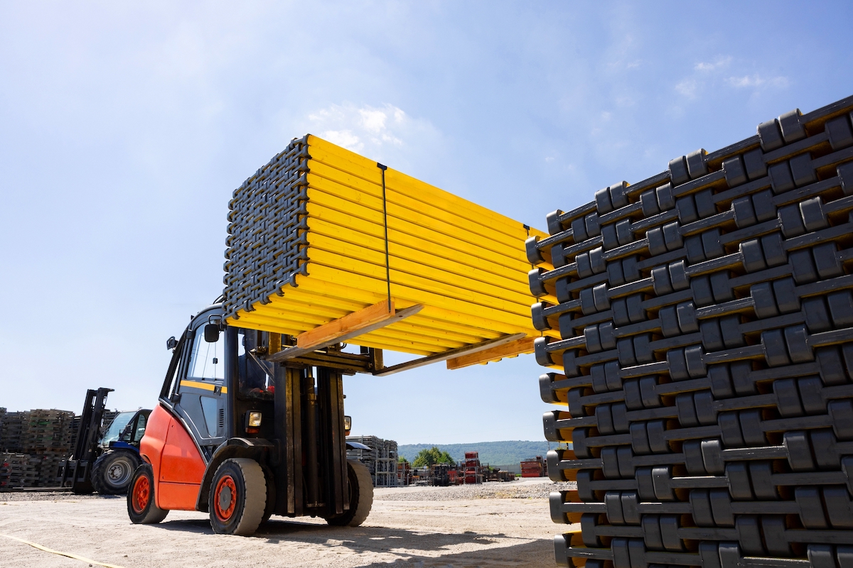 Heavy-duty forklift lifting bundle of yellow scaffolding tubes demonstrating load capacity in construction yard